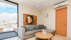 A modern living room with a grey sofa, a round wooden coffee table, and a large window offering a city view. - Penthouse A-Nah by Stella Rentals (Playa del Carmen)