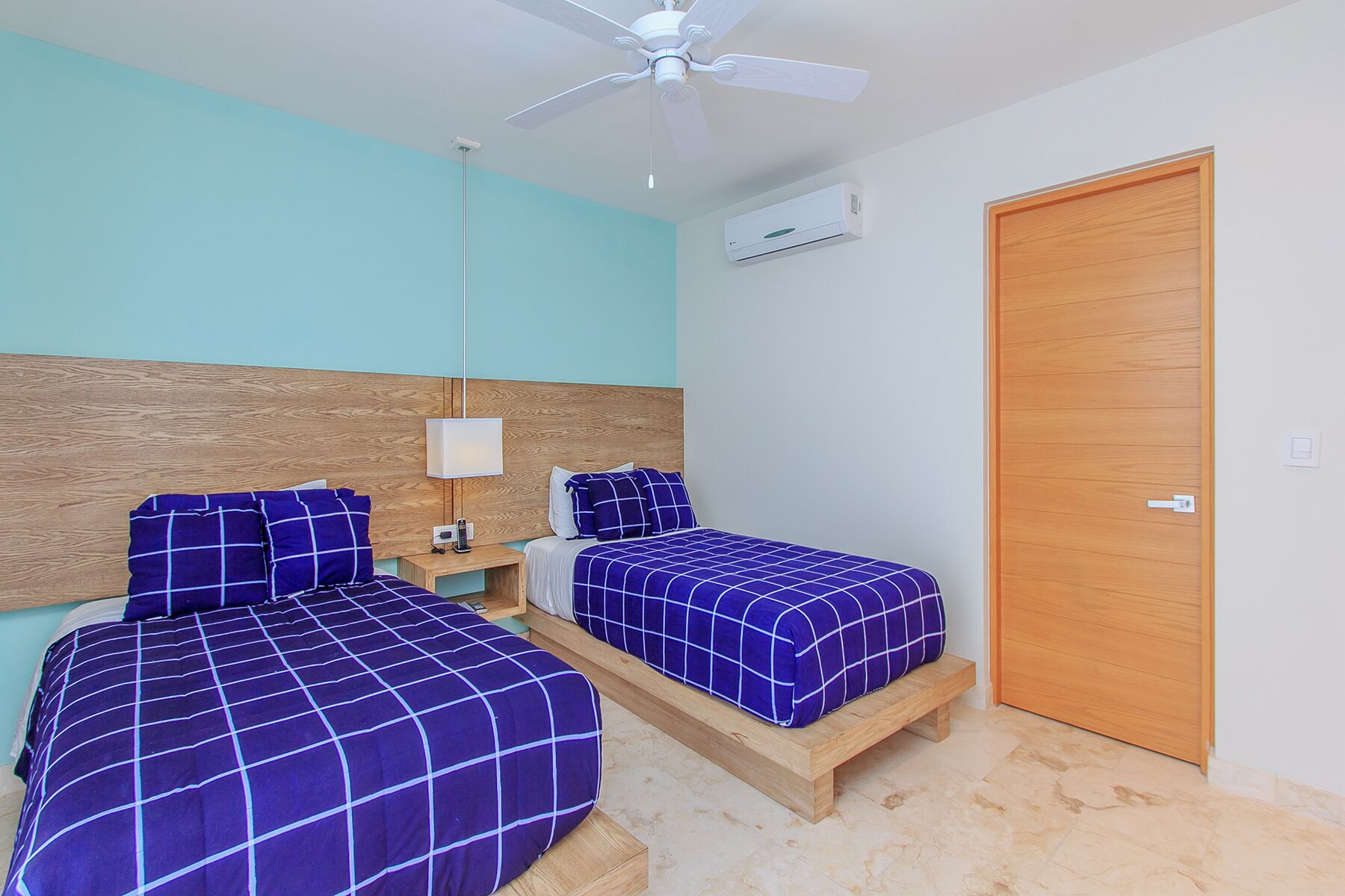 A bedroom with two beds, a ceiling fan, an air conditioning unit, and a wooden door.