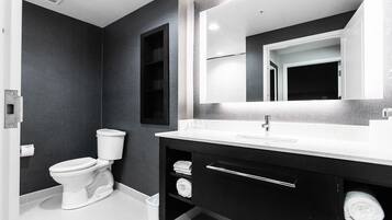 A modern bathroom with a white toilet, dark walls, a large mirror, and a white sink with a silver faucet.
