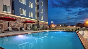 A swimming pool with lounge chairs and umbrellas, a brick wall, and a modern building in the background. - Residence Inn by Marriott Tulsa Midtown (Tulsa)