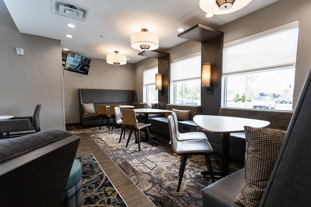 A modern hotel room with a large window, a flat-screen TV, and a seating area with tables and chairs.