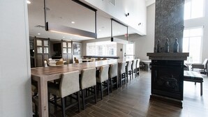 A modern dining area with a long wooden table and chairs, a stone fireplace, and a view of the city through large windows. - Residence Inn by Marriott Tulsa Midtown (Tulsa)