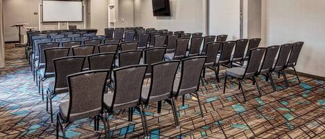A conference room with rows of chairs, a projector screen, and a carpeted floor.