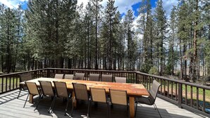 Een terras met een houten tafel en stoelen, omringd door hoge dennenbomen.