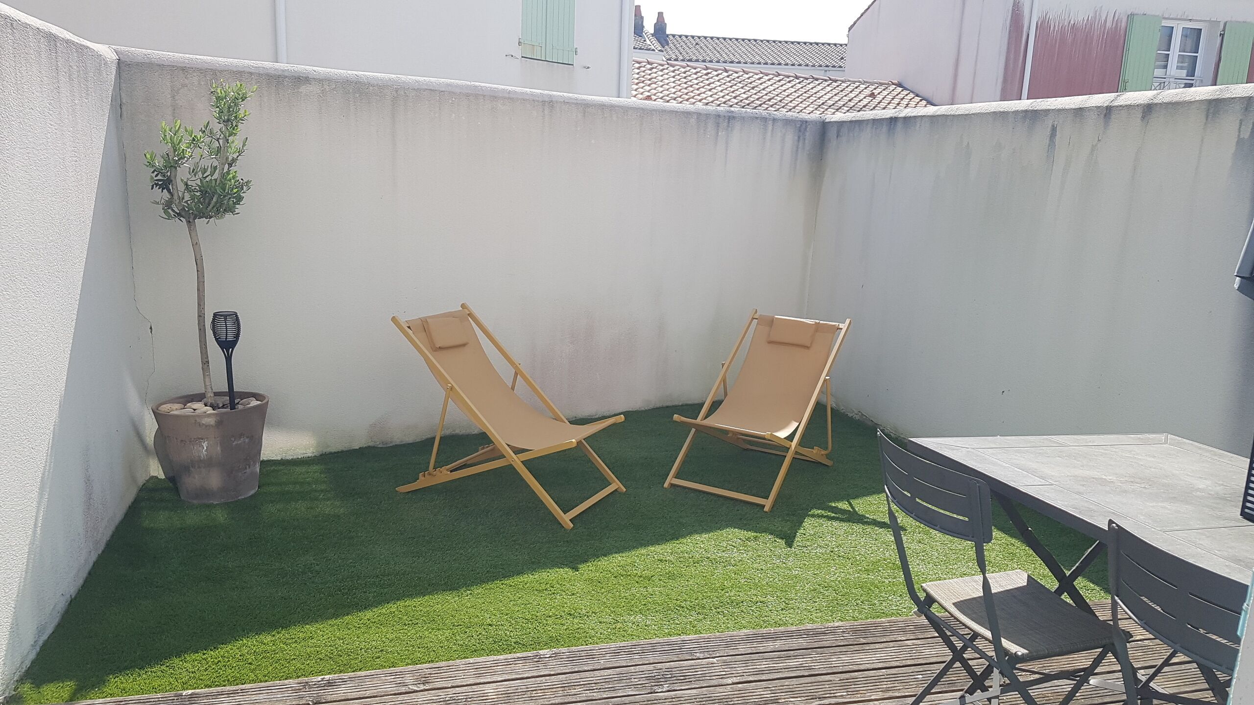 Un petit patio extérieur avec deux fauteuils de jardin en bois, une petite table et un pot de fleurs.