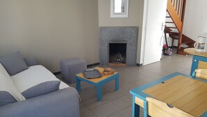 A living room with a sofa, ottoman, and a small table with a basket. A fireplace is visible in the background. - Vacation atmosphere - House - Swimming pool - Île de Ré (La Flotte en Ré)