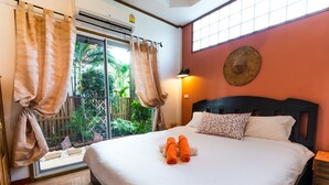 A neatly made bed with two rolled towels, a window with curtains, a wall-mounted lamp, and a decorative wall piece. - Villa Siam Lanna, private pool near the beach with sea view (koh lanta)