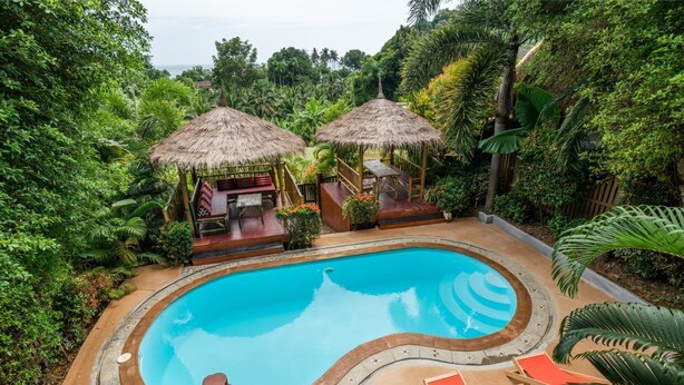 A swimming pool surrounded by lush greenery, with a wooden deck and lounge chairs. - Villa Siam Lanna, private pool near the beach with sea view (koh lanta)