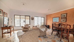 Uma sala de estar com piso estampado em pedra, dois sofás, uma mesa de jantar com cadeiras e janelas amplas com grades de metal.