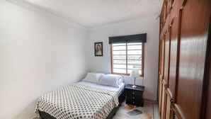 Quarto com cama, mesa de cabeceira, janela e guarda-roupa.