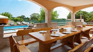 An outdoor dining area with a pool, wooden benches, and a view of the surrounding landscape. - Beautiful modern villa in a small village near the sea (Trget)