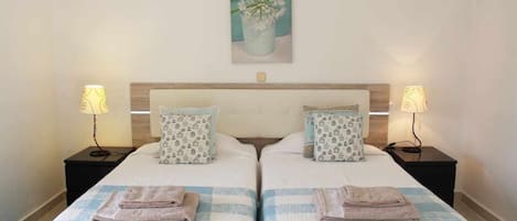 Une chambre double avec deux lits, chacun étant équipé d’un oreiller et d’une table de chevet avec une lampe.