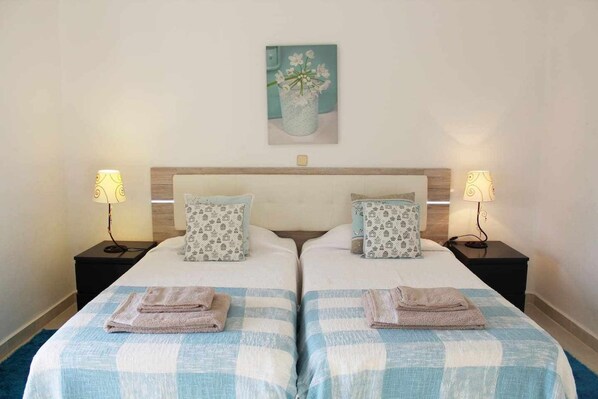 Une chambre double avec deux lits, chacun étant équipé d’un oreiller et d’une table de chevet avec une lampe.