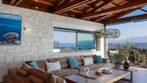 A modern living room with a stone wall, large windows, a wooden ceiling, and a view of the mountains.