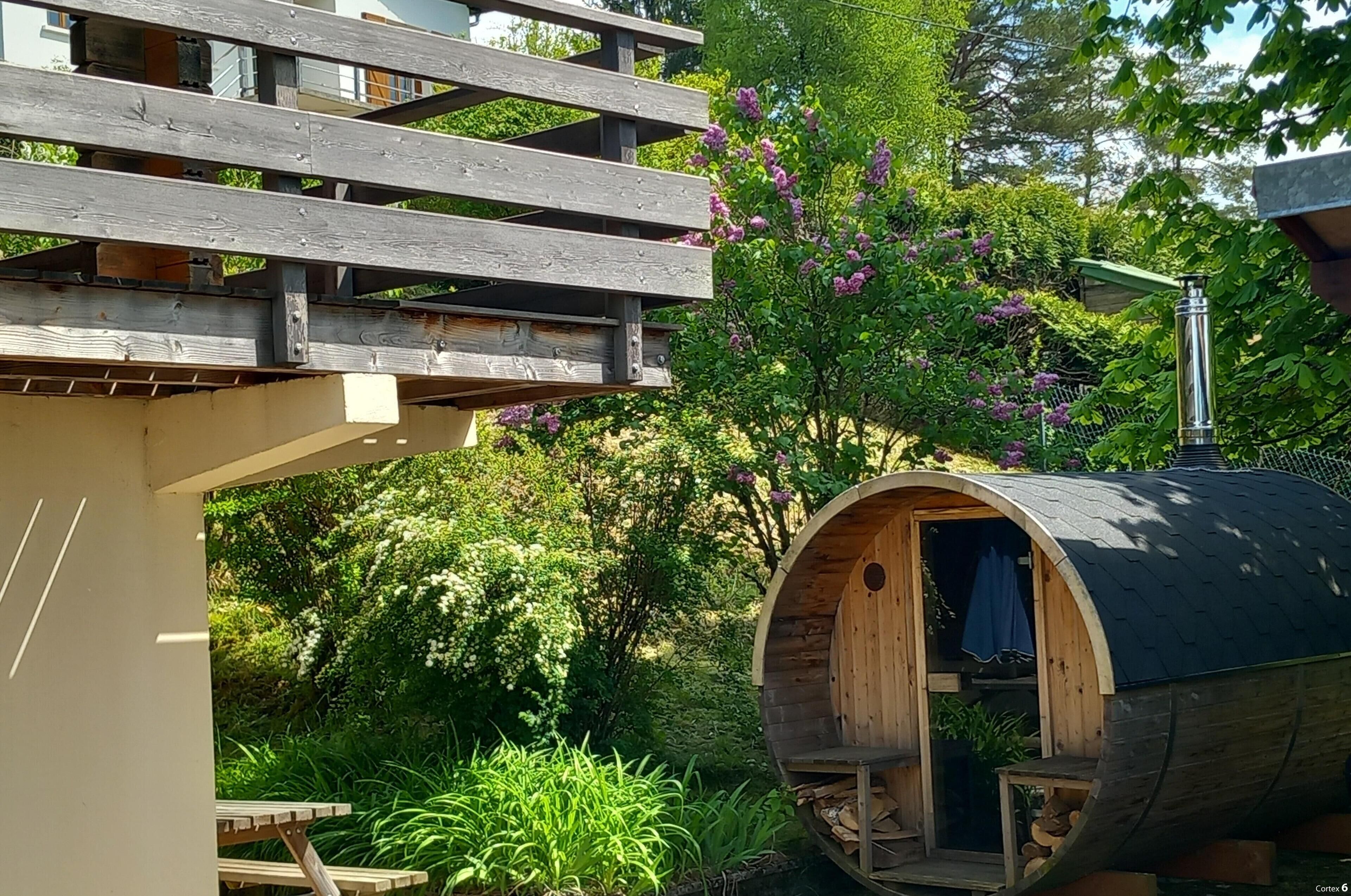 A wooden structure with a barrel-shaped room, a wooden deck, and a garden with flowering plants.