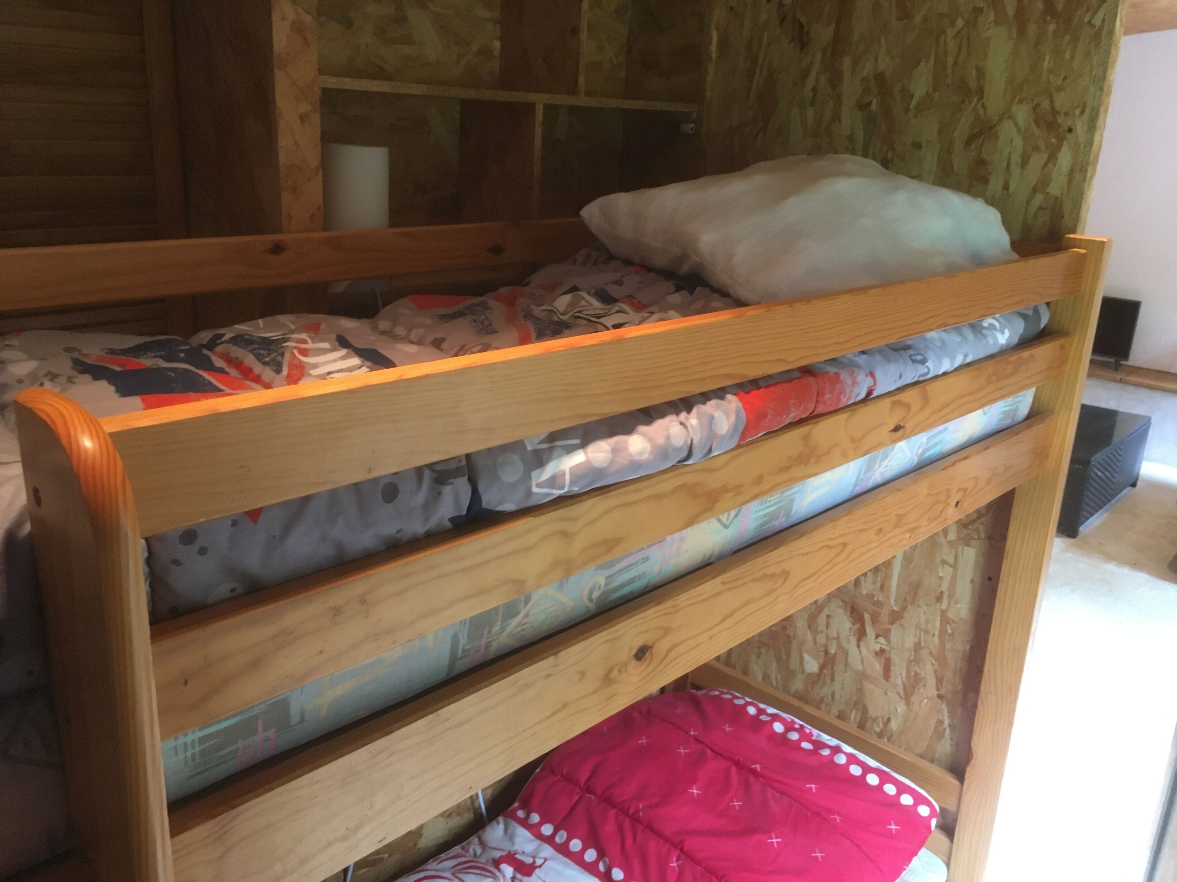 A bunk bed with a wooden frame and a mattress with a patterned blanket.