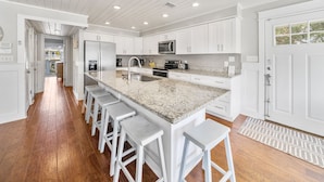 A modern kitchen with white cabinetry, a granite countertop, and stainless steel appliances. There are bar stools along the counter and a large window providing natural light. - Joanna House! Seagrove Beach Cottage, Private Pool, Spacious, close to Seaside. (Seagrove Beach)
