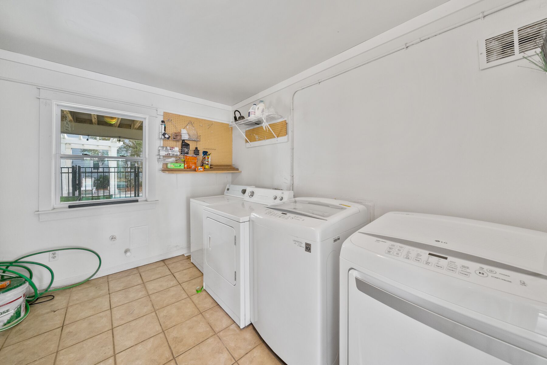 A laundry room with two washing machines, a drying machine, a window, and a pegboard with various items.