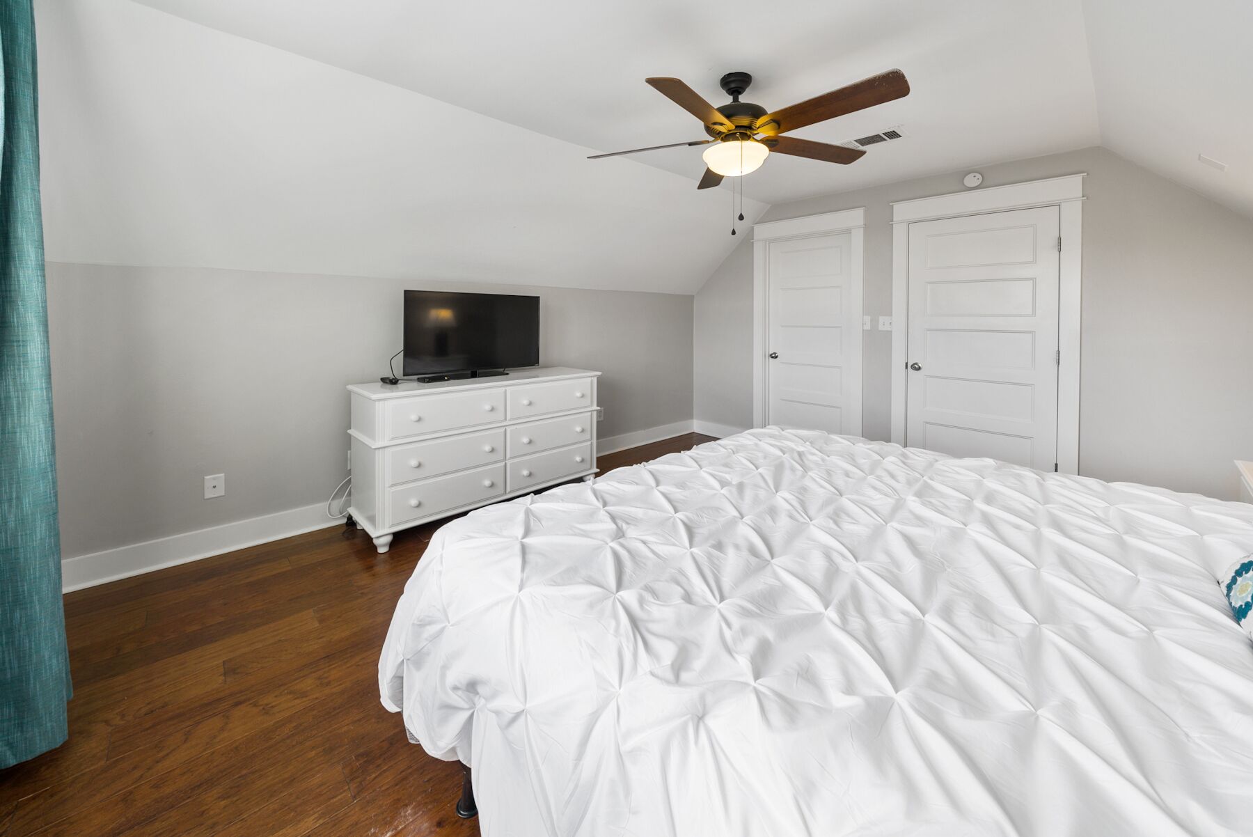 Une chambre à coucher avec un grand lit, une commode, un téléviseur posé dessus et un ventilateur de plafond.