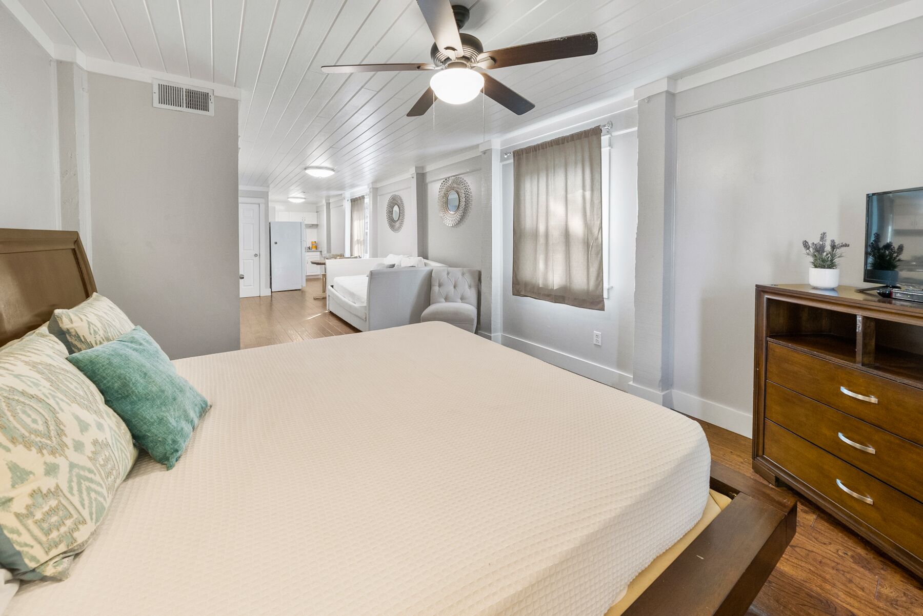 Un dormitorio con una cama grande, ventilador de techo, televisión y cómoda de madera.