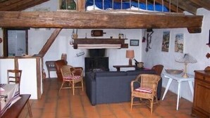 A rustic room with a lofted sleeping area, a fireplace, and a dining table with chairs. - Stylish, Basque sheepfold, all comfort (Pyrénées-Atlantiques)