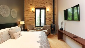 Un dormitorio con una cama grande, dos sillones, un televisor, una chimenea y una pared de ladrillo.