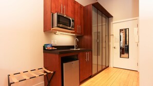 Una cocina compacta con armarios de madera, microondas integrado, refrigerador y un escurreplatos.