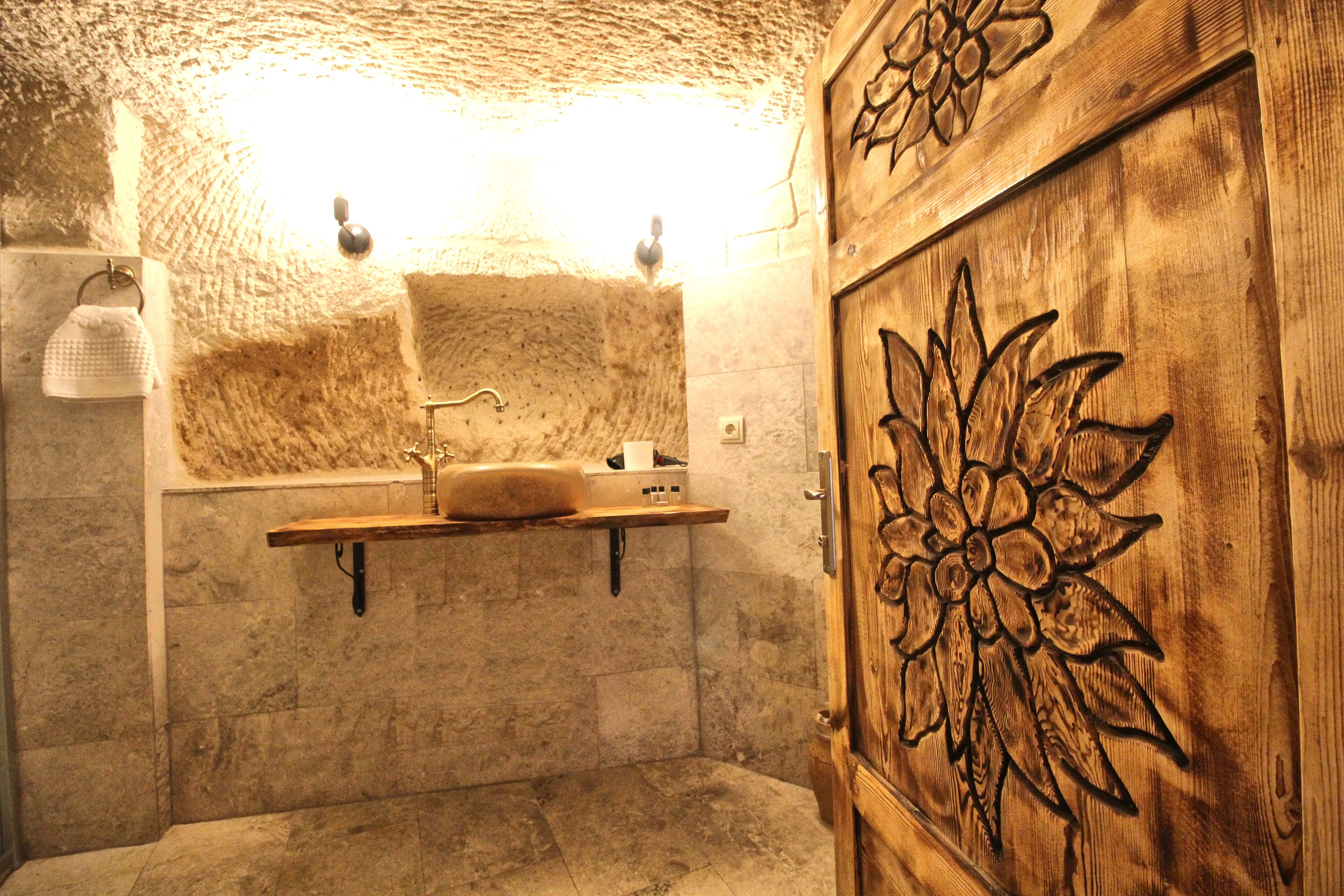 A rustic bathroom with a stone wall, a wooden door with a floral design, and a shelf-mounted sink.