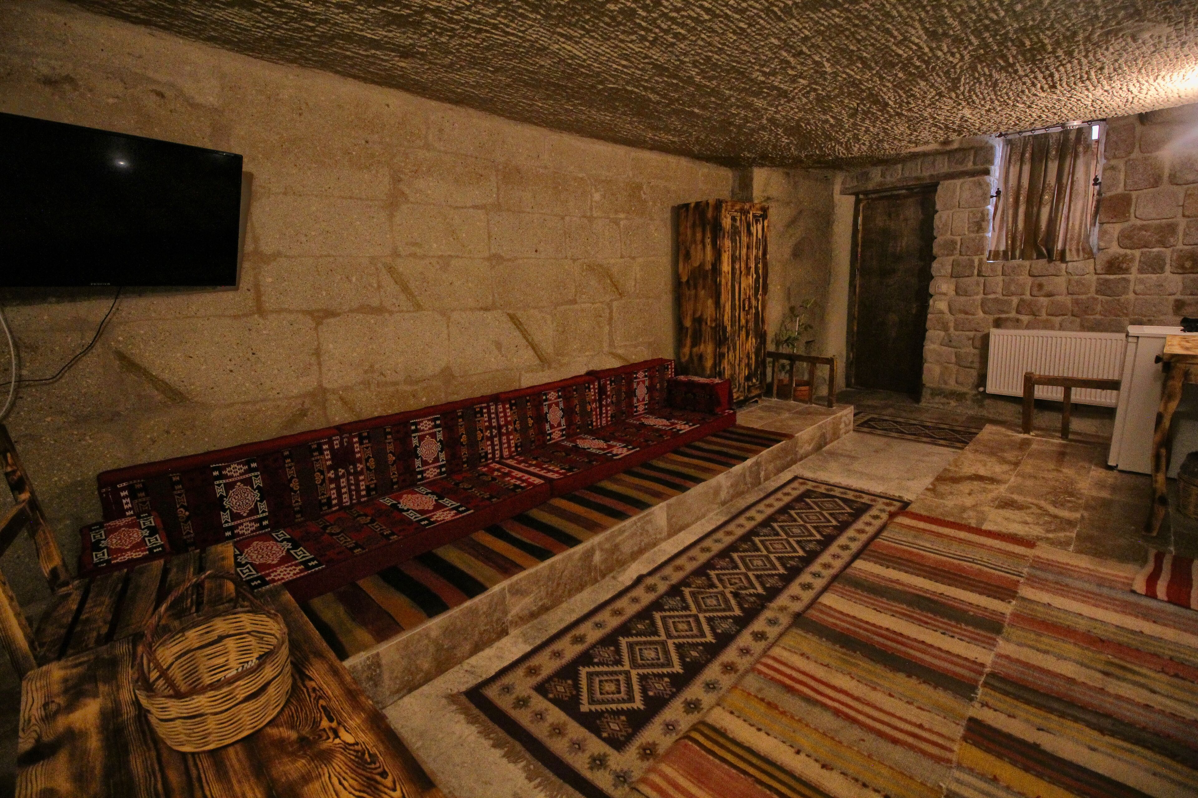 A stone-walled room with a wooden bench, patterned rugs, and a television mounted on the wall.