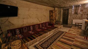A stone-walled room with a wooden bench, patterned rugs, and a television mounted on the wall.