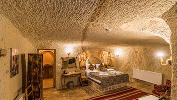A stone-walled room with a bed, a wooden bench, a small table, and a radiator.