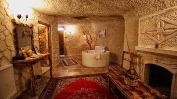 Una habitación rústica con paredes de piedra, un banco de madera, un tapete rojo estampado, una chimenea de piedra y una bañera redonda.