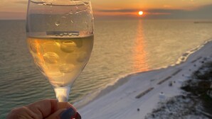 Een hand die een wijnglas vasthoudt, met een zonsondergang boven een strand.