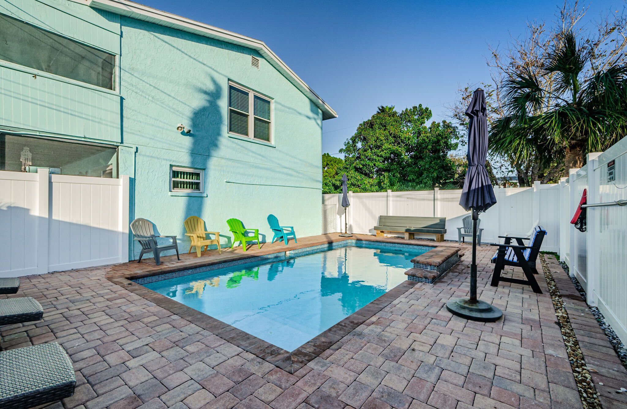 A backyard with a swimming pool, patio furniture, and a house with a light blue exterior.