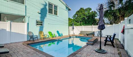 A backyard with a swimming pool, patio furniture, and a house with a light blue exterior.
