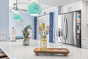 A kitchen with a stainless steel refrigerator, a wine bottle on a tray, and a hanging light fixture.