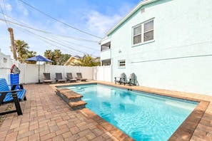 A swimming pool with a tiled edge, lounge chairs, and a white building with windows.