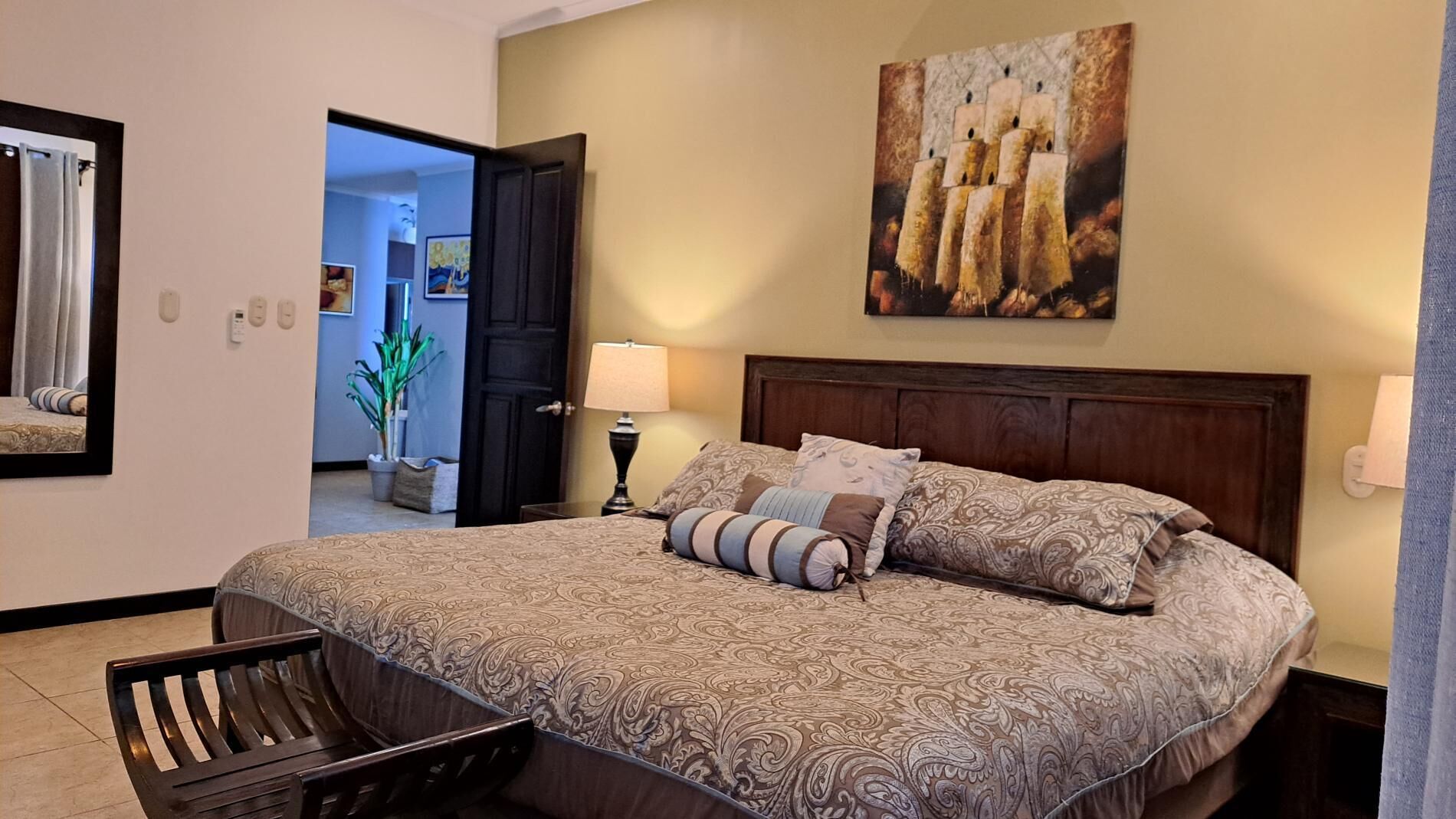 Une chambre d’hôtel avec un grand lit, une table de chevet avec une lampe, un banc en bois et un tableau au mur.