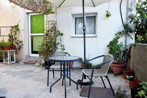 Ein kleiner Patio-Bereich mit einem runden Tisch und zwei Stühlen, umgeben von Blumentöpfen und einer weißen Mauer.