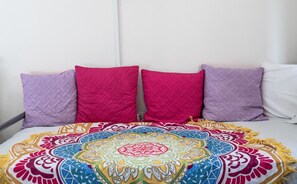 Ein Bett mit einer farbenfrohen, gemusterten Tagesdecke und vier Kissen in Lila- und Pinktönen.