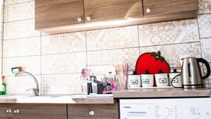Een keuken met houten kastjes, betegelde vloer, een roestvrijstalen waterkoker en diverse keukenspullen op het aanrecht.