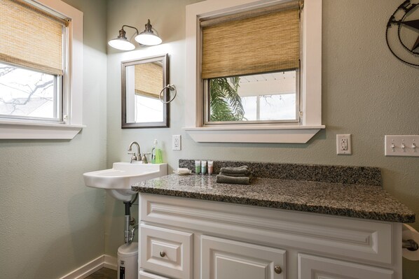 A bathroom with a sink, mirror, vanity, and windows with blinds.