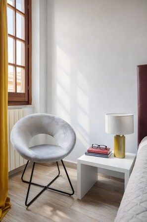 A modern bedroom with a white chair, a bedside table with a lamp, and a window with curtains. - URBANA 37 MAISON   RIONE MONTI. (Roma)