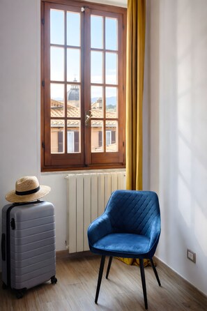 A room with a window, a chair, a suitcase, and a radiator. - Two Bedroom Apartment (Roma)
