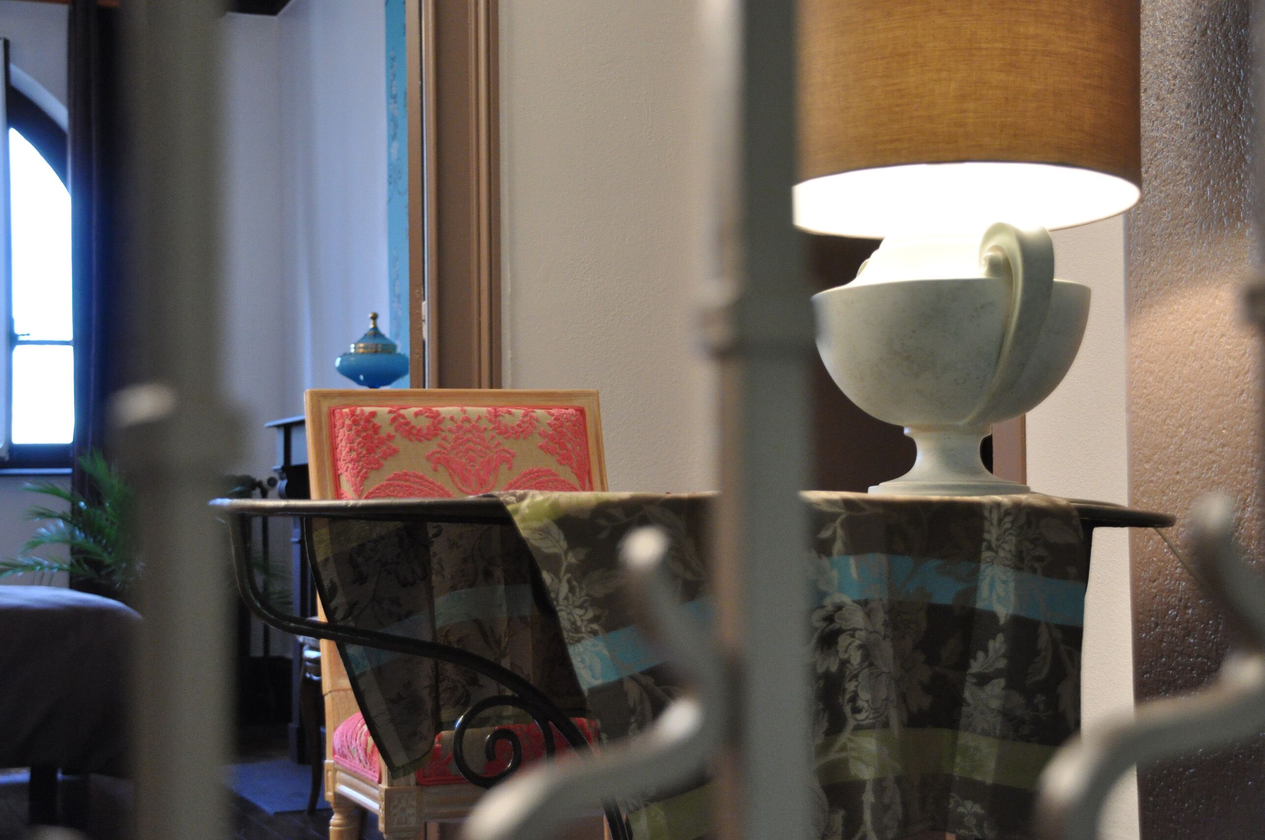 A room with a table lamp, a decorative bowl, and a chair with a floral tablecloth.