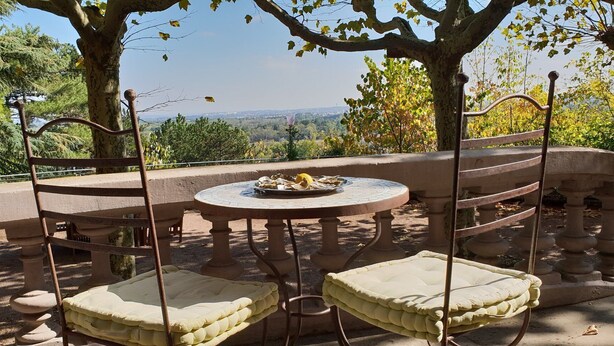 An outdoor seating area with a round table and two cushioned chairs, surrounded by a stone balustrade.
