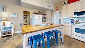 A kitchen with a wooden island, blue bar stools, a refrigerator, and a microwave.
