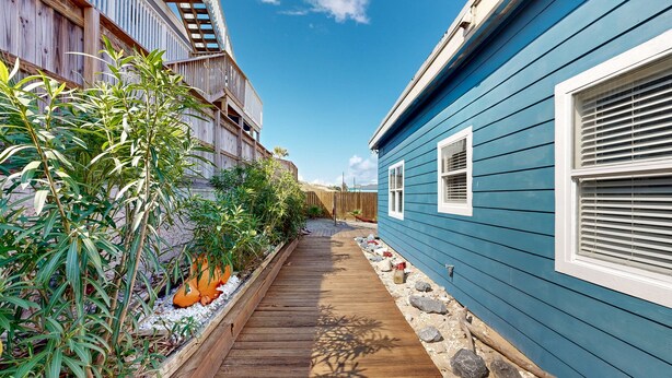 A narrow wooden pathway flanked by a blue house and a wooden fence.