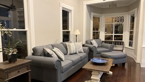 Una sala de estar con un sofá gris, un sillón a juego y una mesa de centro de madera. Hay una planta en maceta sobre una mesita auxiliar.