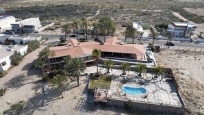 Una casa grande con piscina, rodeada de palmeras y un paisaje desértico.